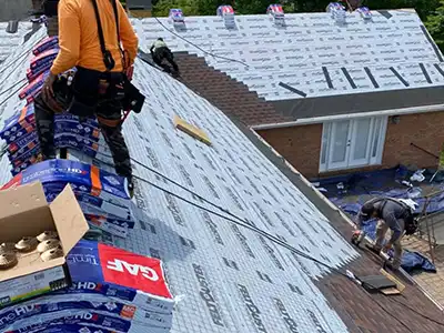 Hollis Roofing & Restoration workers installing new dark red GAF shingles on a home