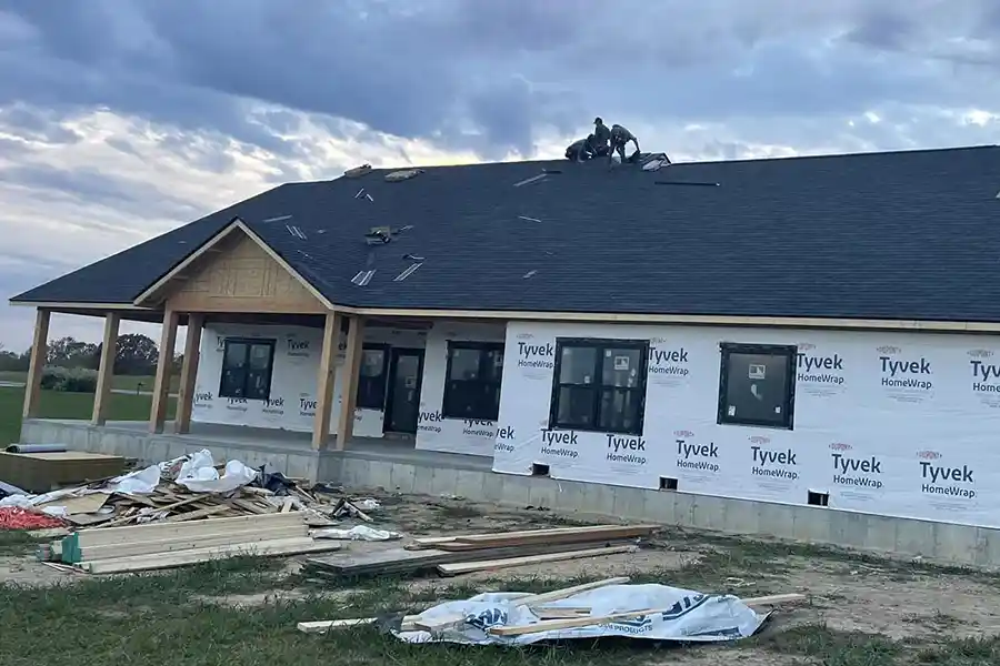 Hollis Roofing & Restoration crew installing new black shingles on a new construction home